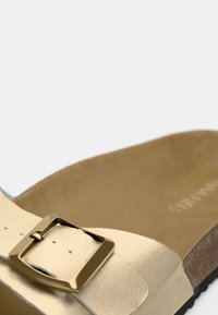 Ανοιχτό μπεζ σανδάλι με μεγάλη μεταλλική τετράγωνη αγκράφα στο λουρί και διαμορφωμένη καφέ φελλόσολα.