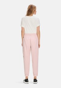 Light pink jogger pants with elastic waistband and cuffs. Soft material, side pockets, paired with a white t-shirt. Black sneakers with print.