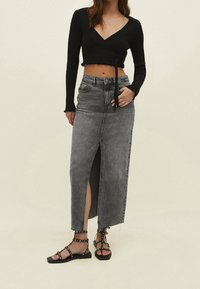 Black ribbed crop top with a V-neck, paired with a gray denim maxi skirt featuring a front slit and frayed hem. Black studded sandals.