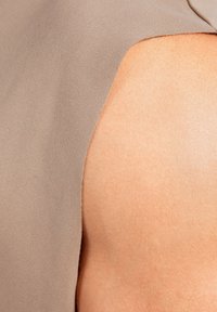 Ärmelloses Oberteil aus weichem Taupe-Stoff, das durch eine glatte Textur und ein dezentes Ausschnittdetail an der Schulter besticht, das einen Hautton darunter zeigt.