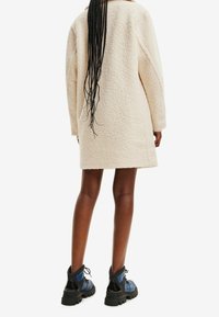 Manteau teddy crème texturé, coupe décontractée avec épaules tombantes, associé à des bottines à lacets noires et bleues.