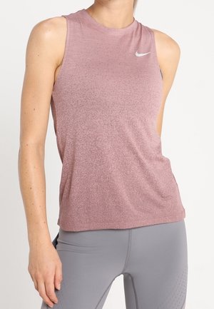 Haut de sport rose sans manches Nike porté avec des leggings gris clair ajustés sur une personne debout sur un fond uni.