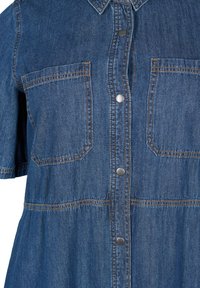 Denim-mekko lyhyillä hihoilla, tummansininen väri, kaksi etutaskua ja hopeiset nepparit, erottuvaa tikkausta ja löysä istuvuus.