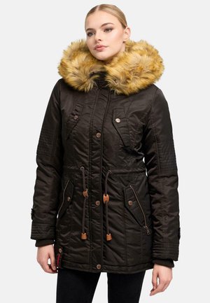 Donna che indossa una giacca invernale trapuntata nera con un ampio cappuccio in pelliccia sintetica beige e tasche frontali, in piedi davanti a uno sfondo semplice.