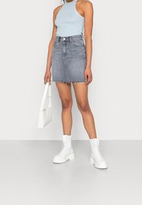 Denim miniskørt med en frynset kant, parret med en lyseblå ærmeløs top og hvide chunky snørebåndsstøvler, og holder en hvid håndtaske.