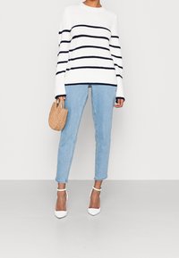Weiß gestreifter Pullover mit Marineblauen Streifen, hellblaue Jeans und weiße High-Heels. Die Accessoires umfassen eine geflochtene beige Handtasche.