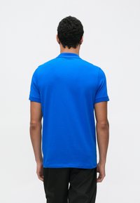 Modra polo majica iz bombaža, s klasičnim ovratnikom, kratkimi rokavi in gladko teksturo, pogled zadaj.