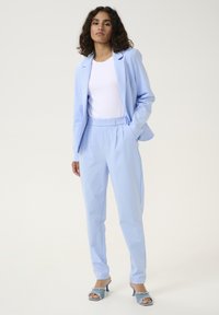 Blazer su misura azzurro chiaro e pantaloni coordinati in tessuto liscio, abbinati a una maglia bianca attillata e sandali con tacco azzurro chiaro.