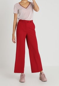 Røde, vide bukser parret med en lyserød v-hals top med skinnende detaljer. Sættet er fuldendt med lyserøde træningssko.