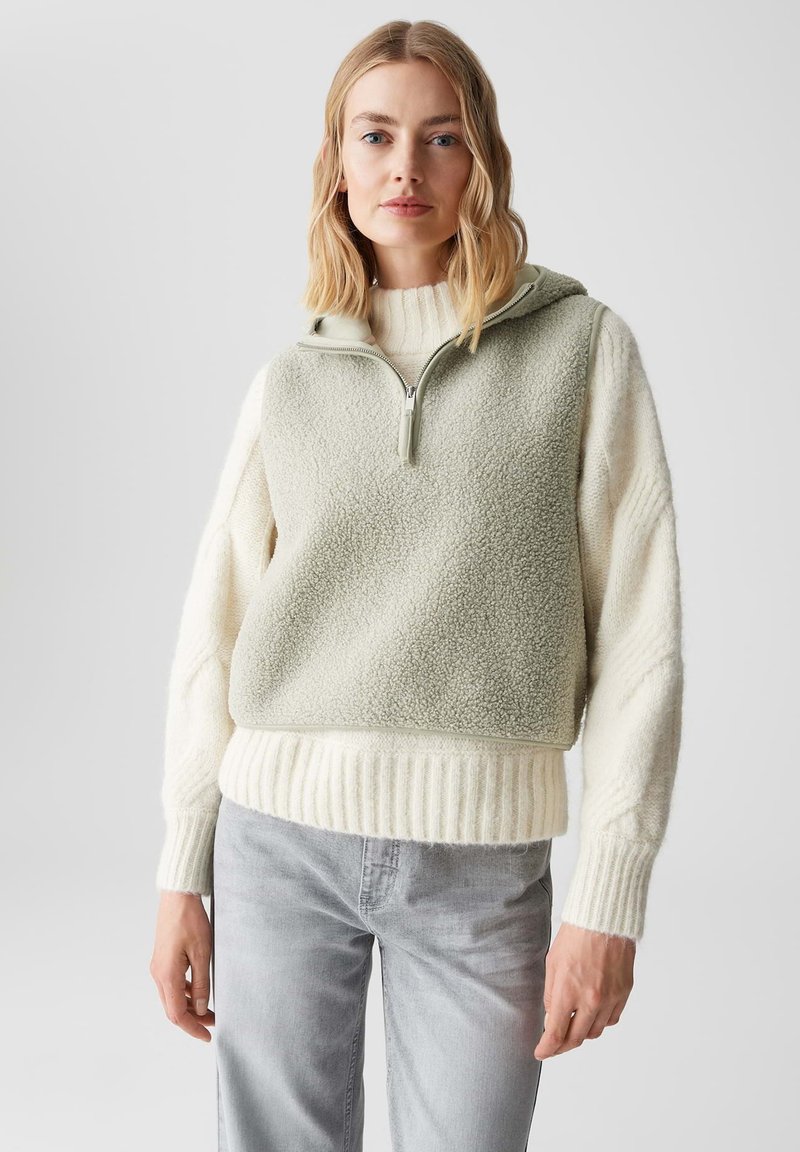 Hellgrüner Fleece-Pullover mit hohem Kragen und Reißverschluss, kombiniert mit einem cremefarbenen, gerippten unteren Abschnitt. Verfügt über breite Strickärmel und einen lässigen Schnitt.