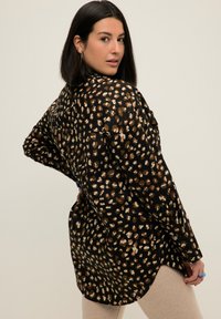 Camicia nera oversize con un motivo leopardato nei toni beige e marroni; maniche lunghe, orlo curvo e tessuto dalla texture morbida.