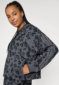 Sweatshirt cinza com padrão de leopardo preto, apresentando um bolso frontal, capuz com cordão e três detalhes em listras nas mangas. Tecido texturizado.
