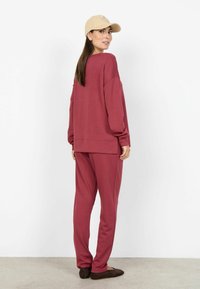 Bluză bordo cu croială lejeră, mâneci lungi și şliţuri laterale, asortată cu pantaloni sport bordoi. Şapcă bej cu detaliu logo.