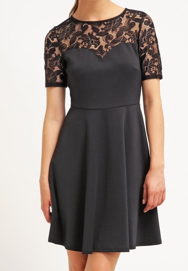 Robe noire avec corsage ajusté et jupe évasée. Superposition en dentelle avec motif floral sur les épaules. Manches courtes, texture de tissu lisse.