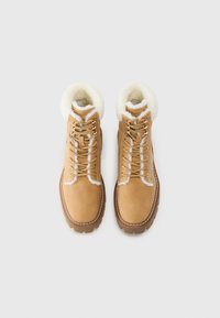 Bottines en cuir beige avec un col en fourrure, dotées d'un matériau en daim beige, de semelles robustes et de détails en couture blanche contrastante.