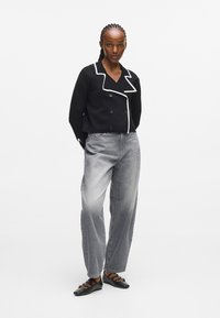 Czarna krótka marynarka z białym wykończeniem, zapinana na podwójne guziki, w połączeniu z jasnoszarymi spodniami w wysokim stanie i czarnymi balerinami.