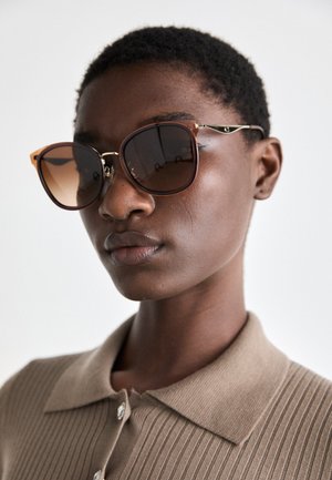 Kattøye solbriller med brune gradient linser, gullakenter og rammer i ambra-farge. Teksturerte stoffkrager i en nøytral nyanse.