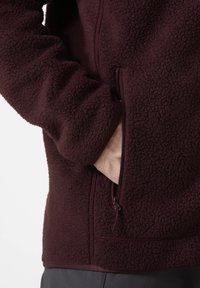 Burgundowa bluza polarowa o miękkiej fakturze, z suwakiem w kieszeni i dopasowanymi mankietami. Posiada wysoki kołnierz i płaskie szwy dla zapewnienia komfortu.