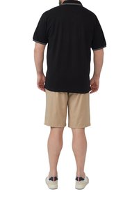 Zwarte polo met korte mouwen en witte kraag en mouwaccenten, gecombineerd met beige shorts. Model draagt lichtgekleurde schoenen.