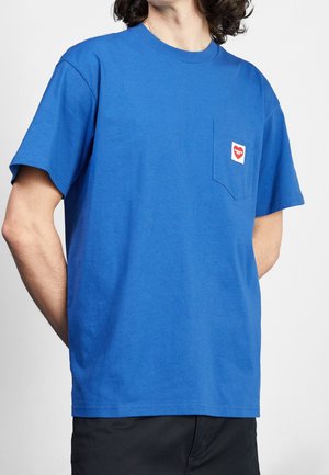 Blaues Baumwoll-T-Shirt mit Rundhalsausschnitt, kurzen Ärmeln und einer Brusttasche auf der Vorderseite, die mit einem roten herzförmigen Logopatch versehen ist.