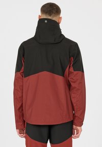 Vattentålig jacka med svart huva och övre del; röd nedre del med ett geometriskt mönster; slät textur och justerbara detaljer.
