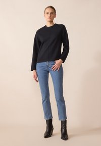 Svart langermet topp med rund hals og en sentral søm, i kombinasjon med lyseblå, tettsittende jeans og svarte høye ankelsko.