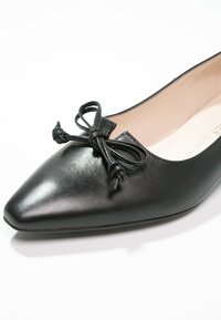 Chaussure plate en cuir noir à bout pointu avec un nœud décoratif noué sur le dessus et une doublure intérieure beige.