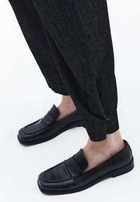 Svarta läderloafers med rund tå, prydda med ett dekorativt band och platt sula, matchade med mörka denimbyxor.