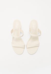 Sandalias de tacón beige con tiras anchas en la parte frontal y en los tobillos. Material sintético suave, diseño de punta aberta y estética minimalista.