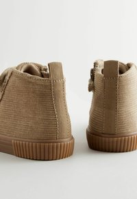 Bottines en tissu marron avec texture côtelée, un bout arrondi et une semelle en caoutchouc. Équipées d'une languette à l'arrière pour un enfilage facile.