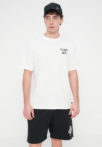 Λευκό κοντομάνικο μπλουζάκι με μαύρο γραφικό κείμενο στο αριστερό στήθος, συνδυασμένο με μαύρο σορτς που έχει λευκή λεπτομέρεια λογότυπου. Μαύρο καπέλο.