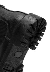 Stivale in pelle nera con pannello in tessuto testurizzato, suola spessa con battistrada, dettaglio in metallo circolare e una finitura liscia sul materiale superiore.