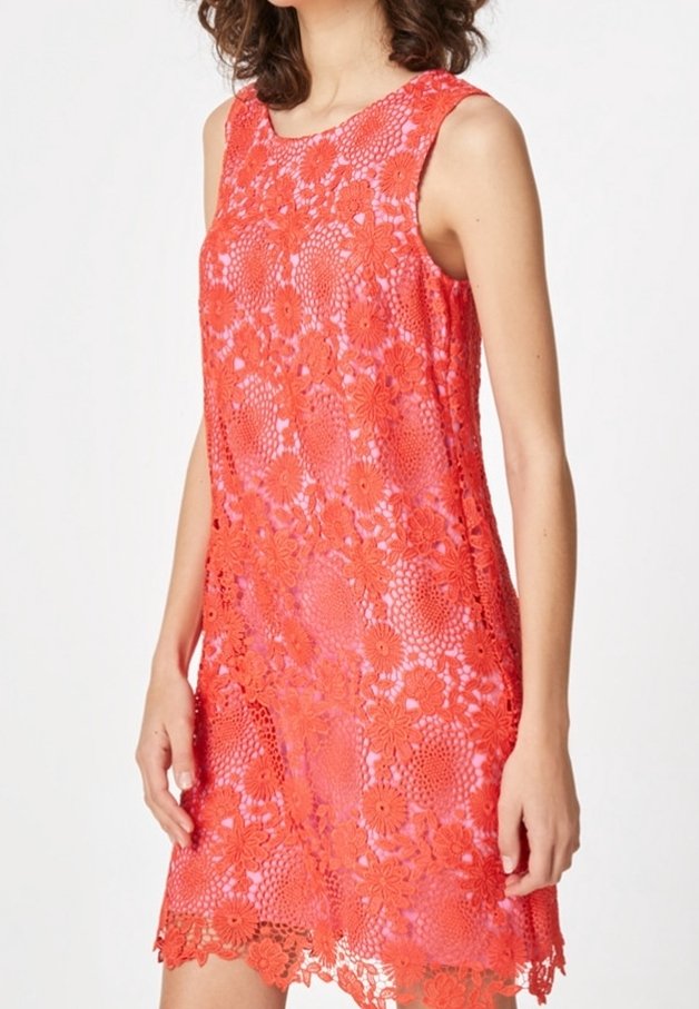 Robe rouge sans manches en dentelle avec motifs floraux portée par une personne debout devant un fond blanc uni.