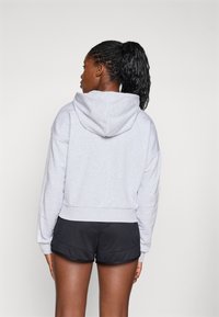 Grå, kort hoodie med teksturert stoff og hette, kombinert med svarte treningsshorts. Har ribbestrikkede mansjetter og livlinning.