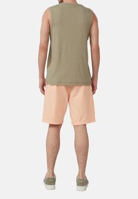 Olivgrünes ärmelloses Top kombiniert mit hellpfirsichfarbenen Shorts, beide aus weichen Materialien. Weiße Sneakers mit dezenten grünen Akzenten.