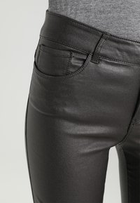 Pantalones skinny de imitación cuero negros con una textura suave, corte ajustado y detalle de bolsillo frontal. Piernas cónicas y diseño de cintura alta.