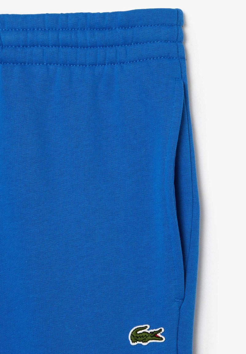 Niebieskie bawełniane dresy z elastycznym pasem, z małym zielonym logo krokodyla haftowanym na dolnej części nogawki.