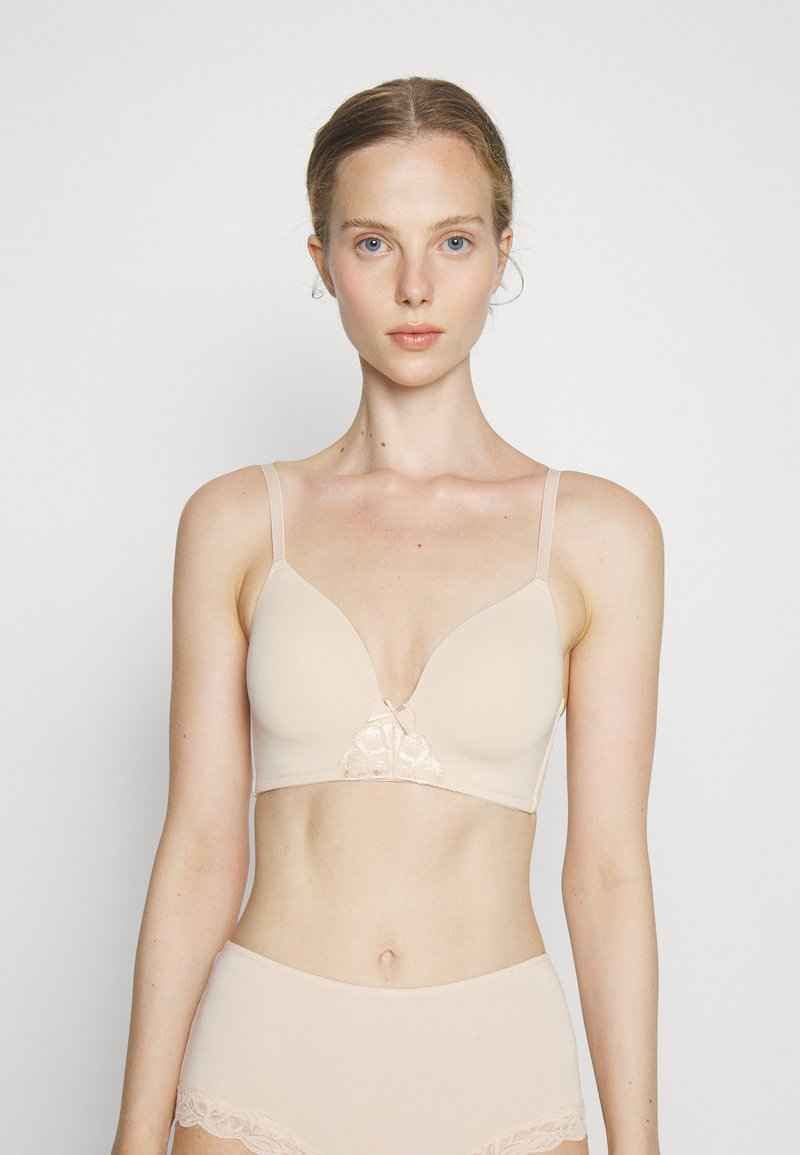 Beige wireless bra featuring a plunging neckline, smooth fabric, adjustable straps, and lace detailing at the center front.