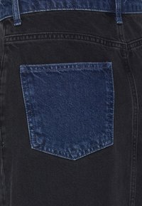 Zwarte denim jeans met een contrasterende blauwe denim achterzak, met zichtbare stiksels en een textuur oppervlak.