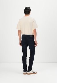 Beige t-shirt med kort ärm, mörka denimjeans och vita sneakers med svarta detaljer. Jeansarna har slim fit och bakfickor.