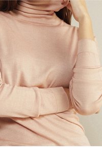 Jasnoróżowy sweter z wysokim kołnierzem, wykonany z miękkiego dzianiny, dopasowany fason z prążkowanymi mankietami. Gładka faktura z delikatnym połyskiem.