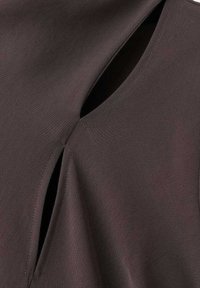 Nahaufnahme eines dunkelbraunen Stoffes mit zwei sich überlappenden Schlitzen, die die Textur und präzise Steppnähte zeigen.