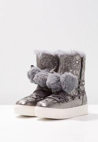 Bottes d'hiver métalliques argentées avec un embossage floral, une bordure duveteuse et des pompons, fermeture éclair sur le côté et semelles blanches à plateforme.
