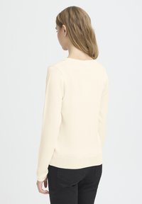 Svetlo béžový sveter s dlhými rukávmi, okrúhlym výstrihom a rebrovaným lemom. Tkanina pôsobí mäkko a má hladkú textúru.