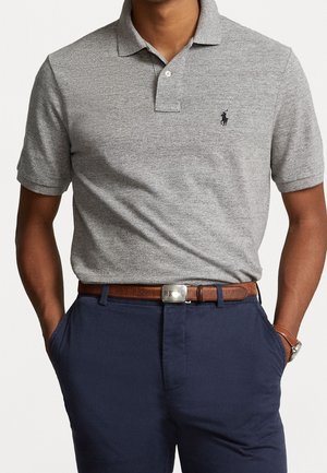 Graues Poloshirt mit Kragen, Knopfleiste mit zwei Knöpfen und gesticktem Logo, kombiniert mit dunkelblauer Hose und braunem Ledergürtel.