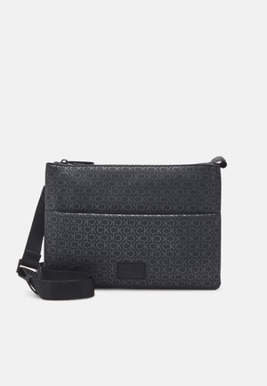 Small black crossbody bag with repeating CK logo pattern and adjustable strap, featuring a front pocket and zipper closure.