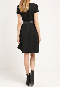 Svart texturerad klänning med korta ärmar, en figurnära midja och en utsvängd kjol. Tillsammans med knähöga svarta klackstövlar.