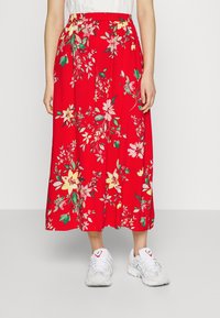 Red floral maxi skirt with an elastic waistband, featuring multi-colored flowers and green leaves. Paired with white athletic sneakers.