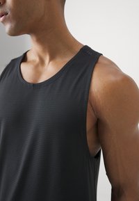 Fekete, ujjatlan sportos trikó, amely finom csíkos textúrájú anyagból készült, kerek nyakkivágással és testhez álló fazonnal rendelkezik.