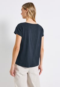 T-shirt à manches courtes bleu foncé avec un col arrondi et une coupe décontractée, fabriqué en tissu doux et léger. Ourlet courbé subtil en bas.